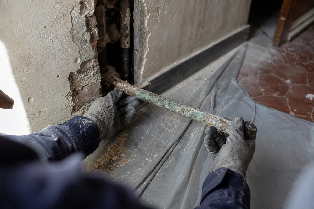 Tube de cuivre percé par corrosion sorti d&rsquo;une cloison ancienne, sol protégé par une bâche