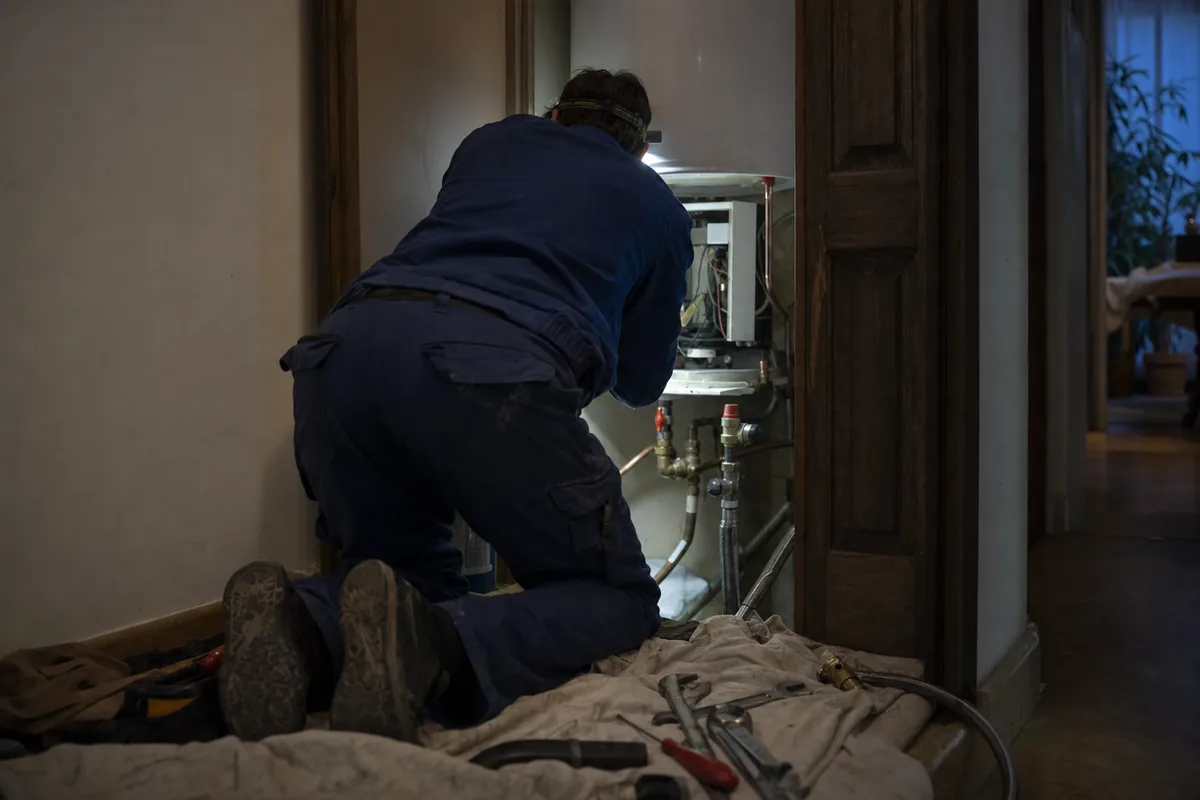 Plombier travaillant à la lampe frontale dans un placard technique le soir